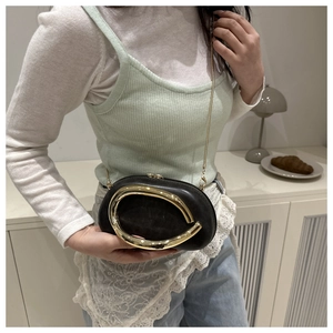 Detail of a chic black oval crossbody bag with a large gold C-ring and metal chain