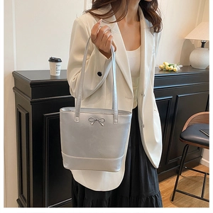 Sac cabas argenté avec nœud métallique porté par un mannequin en tenue de bureau chic