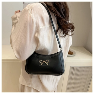 Detail of a vintage black baguette bag featuring a stylish gold metal bow clasp and smooth PU