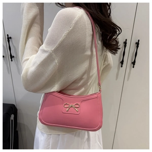 Pink crescent shoulder bag with golden bow detail shown on a female model