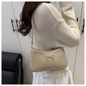 Détail d'un sac à bandoulière beige avec boucle noeud doré sur cuir lisse et souple
