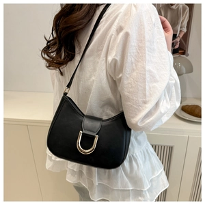 Close-up of minimalist black dumpling bag with gold D-ring buckle worn on the shoulder
