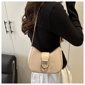 Detail of beige half-moon shoulder bag featuring a large gold U-shaped metal buckle
