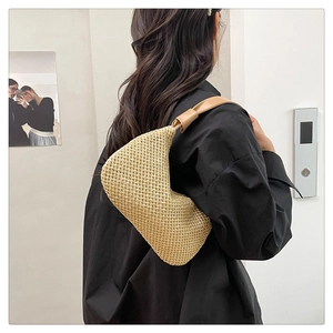 Nahaufnahme der beige geflochtenen Stroh-Halbmondtasche mit braunem Lederriemen am Model