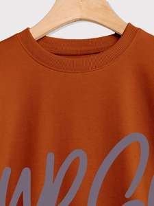 Detail of ribbed crew neck and grey artistic script print on orange sweatshirt