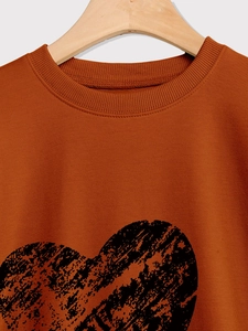Close-up of caramel orange sweatshirt with a distressed black heart print and crew neck