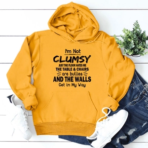 Flat lay of yellow hoodie featuring I'm Not Clumsy text with drawstring and kangaroo pocket