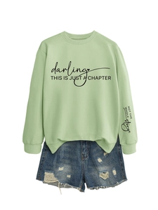 Dettaglio della felpa verde chiaro con stampa 'darling' e pantaloncini di jeans strappati