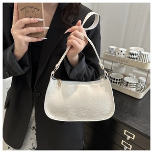 Détail du sac à bandoulière blanc motif crocodile avec boucles dorées sur un blazer noir