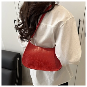 Gros plan sur un sac épaule rouge à motif crocodile montrant la texture du cuir et la sangle