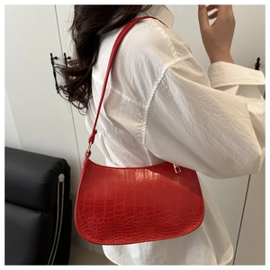 Sac à bandoulière rouge texture crocodile avec fermeture dorée porté par un modèle