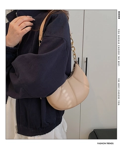 Close-up of beige croissant bag with vertical pleated texture and gold chain strap