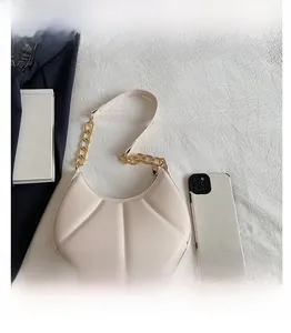 Detail of scalloped quilted hobo bag in cream white with a chunky gold chain strap