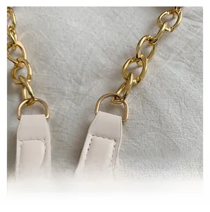 Detail of off-white lychee leather strap with thick gold metal chain and neat stitching