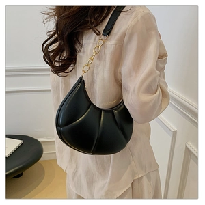 Detail of black crescent shoulder bag featuring vertical quilted texture and gold chain link