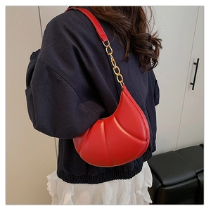 Detail of red crescent quilted shoulder bag with gold chain strap on navy sweatshirt