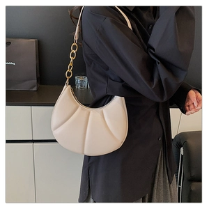 Close-up of beige crescent bag featuring pleated texture and gold chain strap detail