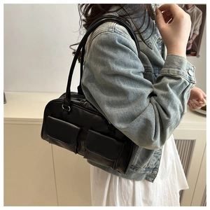 Detail of black glossy shoulder bag with dual pockets worn over a denim jacket