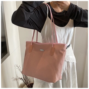 Close-up of pink woven tote bag featuring long straps and minimalist metal logo detail