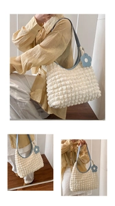 Detail of creamy white bubble textured hobo bag with light blue strap and flower charm