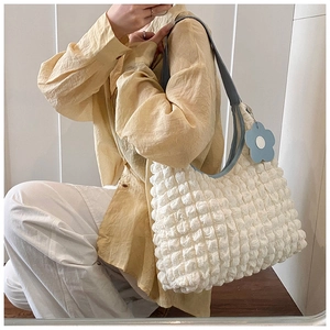 Detail of white bubble texture shoulder bag with blue strap and floral pendant on model