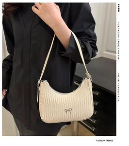 Detail of cream woven crescent bag with metal bow accent shown on shoulder