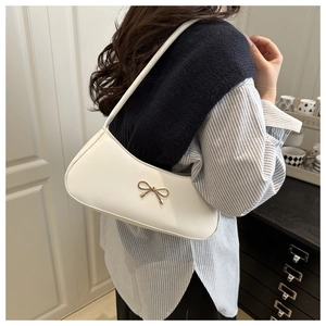 Detailed view of a white underarm bag with a golden bow on a model wearing a striped shirt