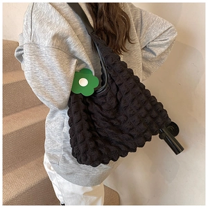 Detail of black cloud-textured tote bag with a green sunflower charm on minimalist stairs
