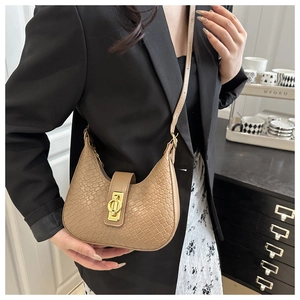 Close-up of khaki crocodile pattern crescent bag with golden twist lock on shoulder