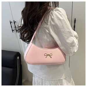 Pink baguette bag with gold bow charm shown worn underarm for size perspective