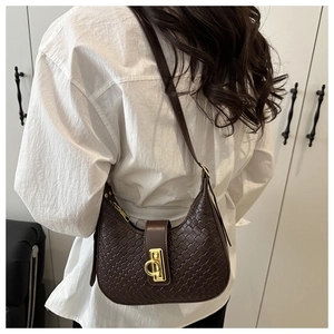 Detail of dark brown woven crescent bag with golden horseshoe buckle worn by a model
