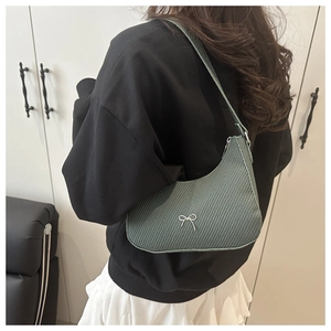 Close-up of green crescent bag featuring woven texture and silver bow detail on shoulder