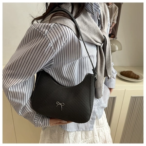 Detail of black woven shoulder bag featuring a decorative silver metallic bow accent