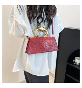 Détail du sac rouge à motif croco avec grande poignée dorée arquée et bandoulière fine