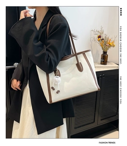 Detail of a large cream tote bag with brown trim and cute plush charm on a model