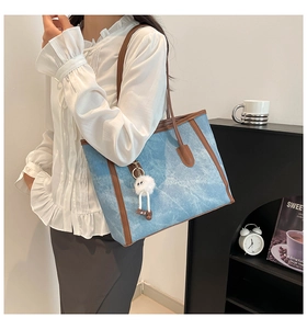 Detailed shot of large denim tote bag with brown leather trim and fuzzy eye charm
