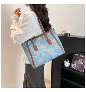 Detail of light blue denim tote bag with brown leather handles worn by a model