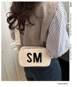 Detail of cream crossbody bag featuring bold SM logo patch and patterned wide strap