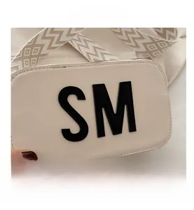 Detail der cremefarbenen Leder-Umhängetasche mit schwarzem SM-Schriftzug und breitem Gurt