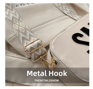 Details von hellgoldenem Metallhaken und verstellbarem Webriemen an cremefarbener Tasche