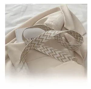 Detail der beigen Tasche mit Chevron-Gurt und großem SM-Buchstabendesign