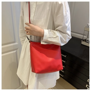Detailed view of a bright red bucket bag styled on a white dress for fashion appeal