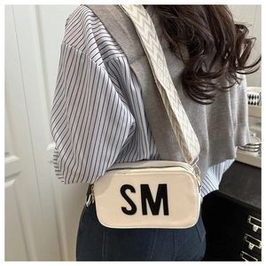 Detail einer stilvollen cremefarbenen Umhängetasche mit SM-Schriftzug am Model