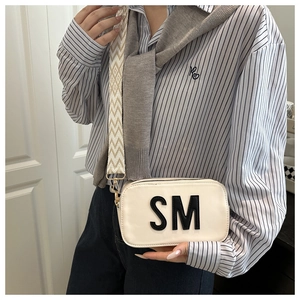 Detail der cremefarbenen Tasche mit SM-Schriftzug und breitem geometrischem Web-Schultergurt