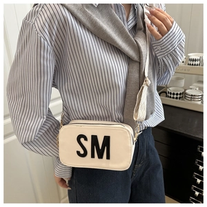 Detail einer schicken cremefarbenen Umhängetasche mit schwarzem SM-Patch und Gurtband
