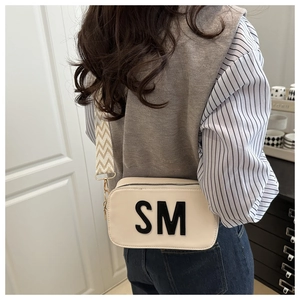 Detail of off-white crossbody bag featuring a wide striped strap and bold SM letter print