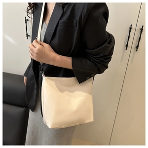 Gros plan d'un sac seau minimaliste en cuir crème avec fine bandoulière sur modèle