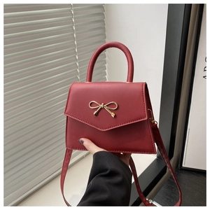 Detail of burgundy textured leather handbag with a golden bow and elegant top handle