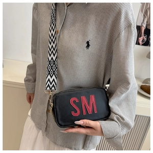 Detail of black crossbody bag featuring a red letter patch and geometric wide strap