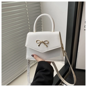 Detail of white square handbag with golden bow hardware and elegant top handle strap